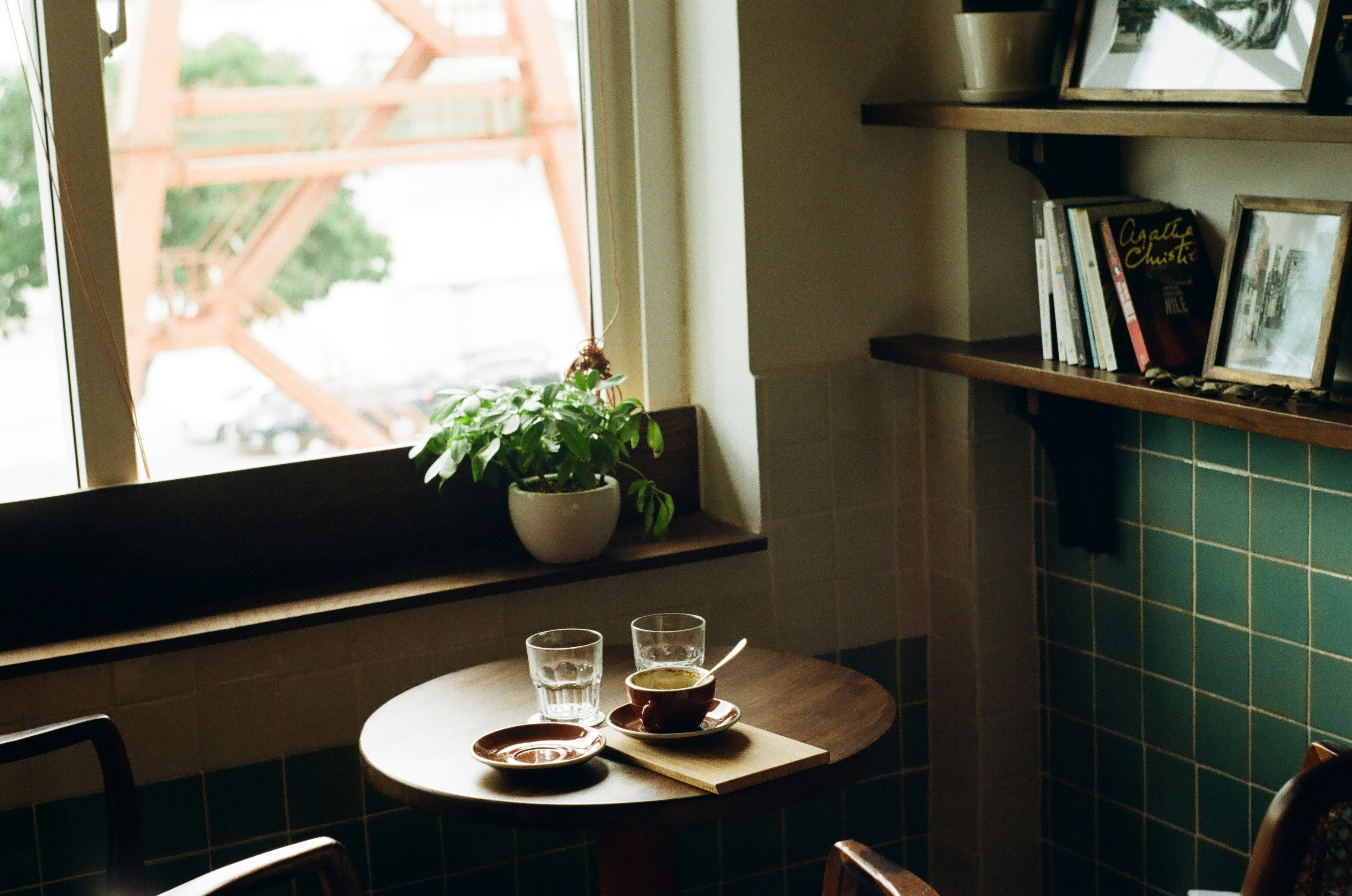 A warm morning scene — coffee on a wooden table, books on a shelf, plant by the window